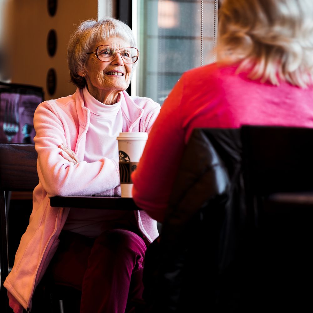 Une femme âgée et une proche prennent le temps de discuter autour d’un café.